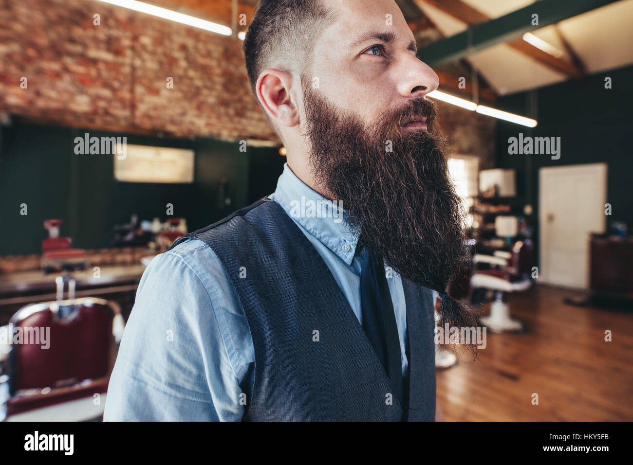 Close up di grave barbiere maschio con la barba lunga. Parrucchiere nel salone di guardare lontano e di pensare. Foto Stock