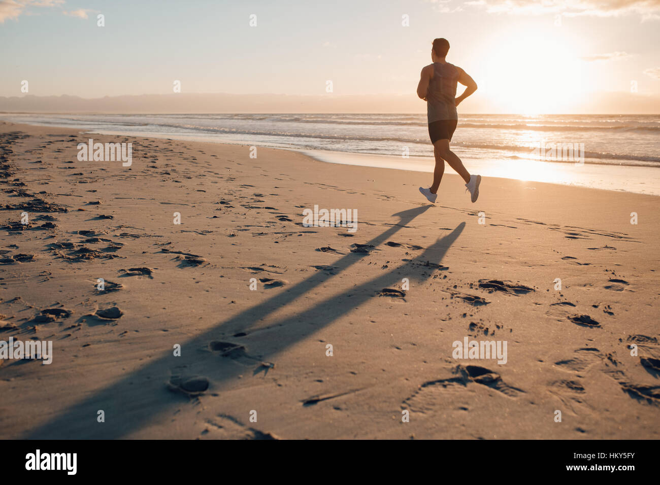 Colpo di montare l'uomo che corre lungo la riva del mare in mattina. Maschio sano jogging sulla spiaggia. Foto Stock