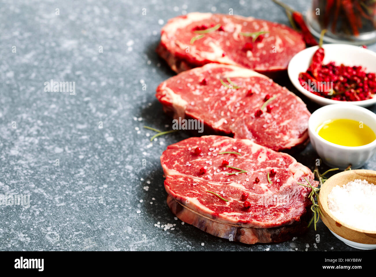 Materie carni fresche Ribeye con rosmarino, pepe e sale marino su pietra ardesia sfondo Foto Stock