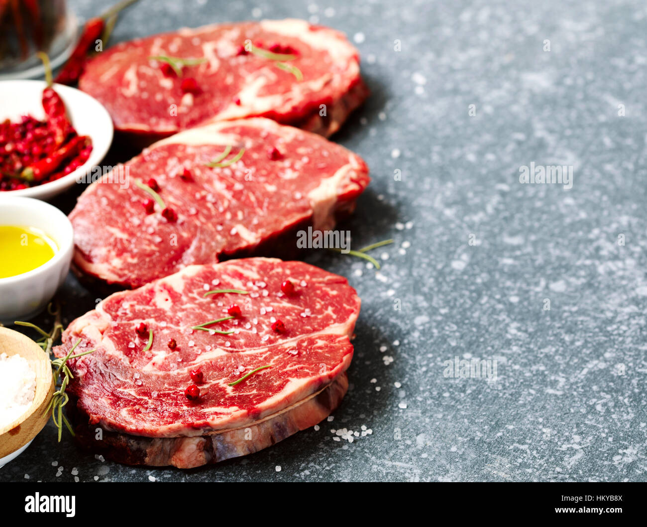 Materie carni fresche Ribeye con rosmarino, pepe e sale marino su pietra ardesia sfondo Foto Stock