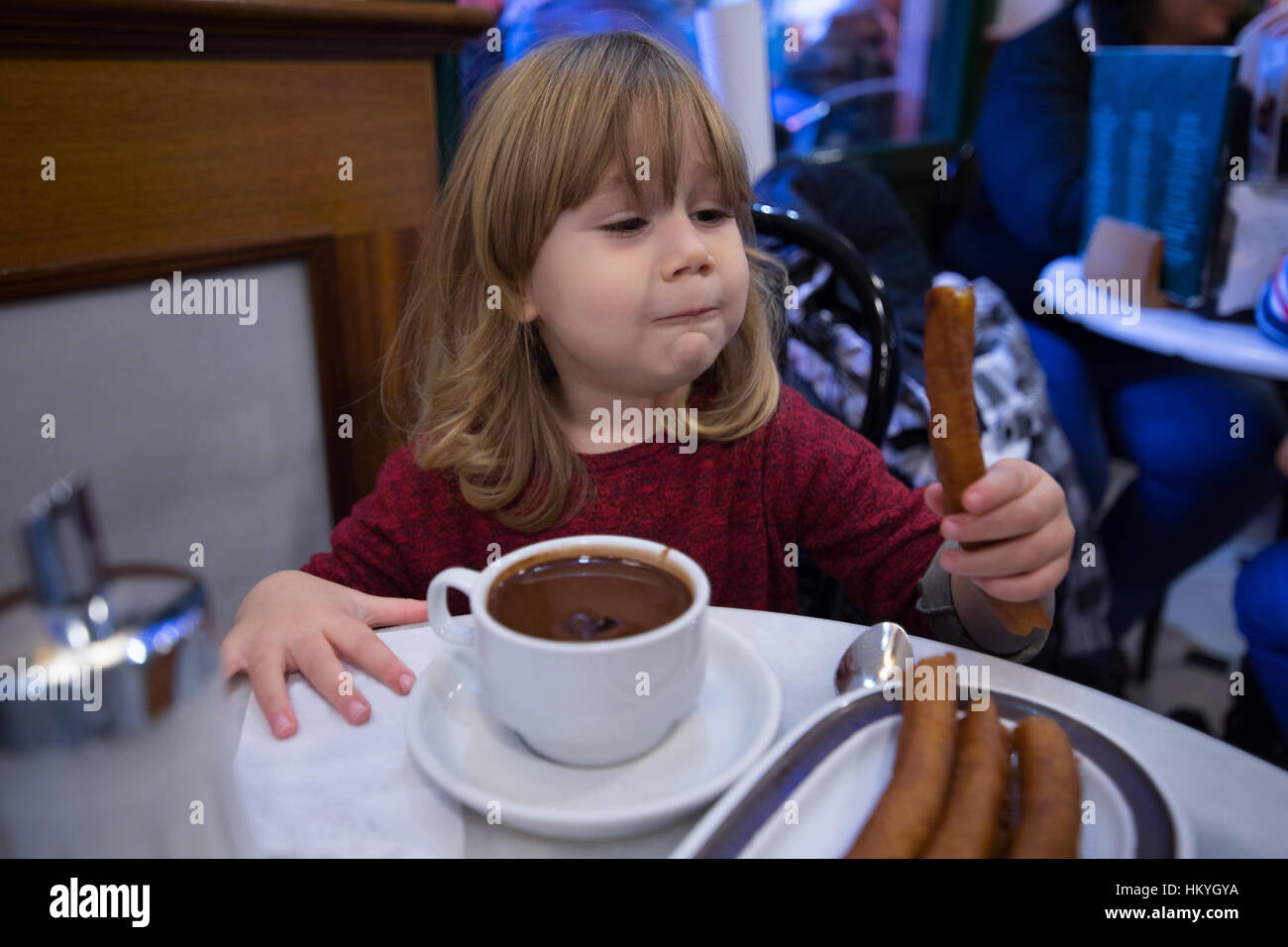Tre anni bambino biondo con maglione rosso mangiare spagnolo baton,  denominato churros o Porras, con il cioccolato in tazza al cafe Foto stock  - Alamy