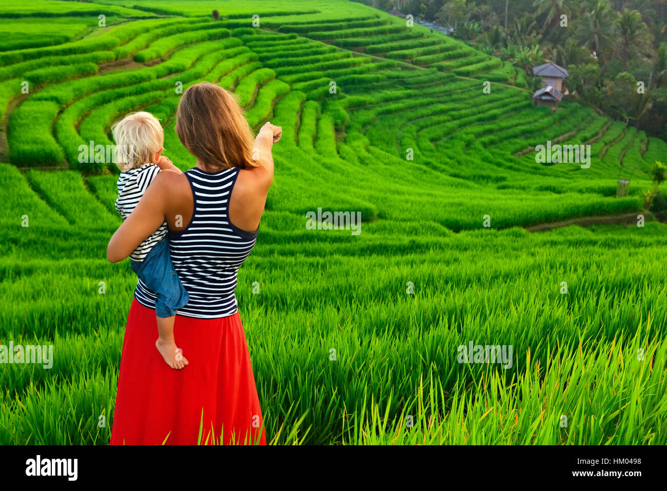 Bella vista dei campi Balinese. La natura a piedi in verdi risaie a terrazza. Felice madre tenere felice piccolo bambino. Viaggiare con bambini Foto Stock