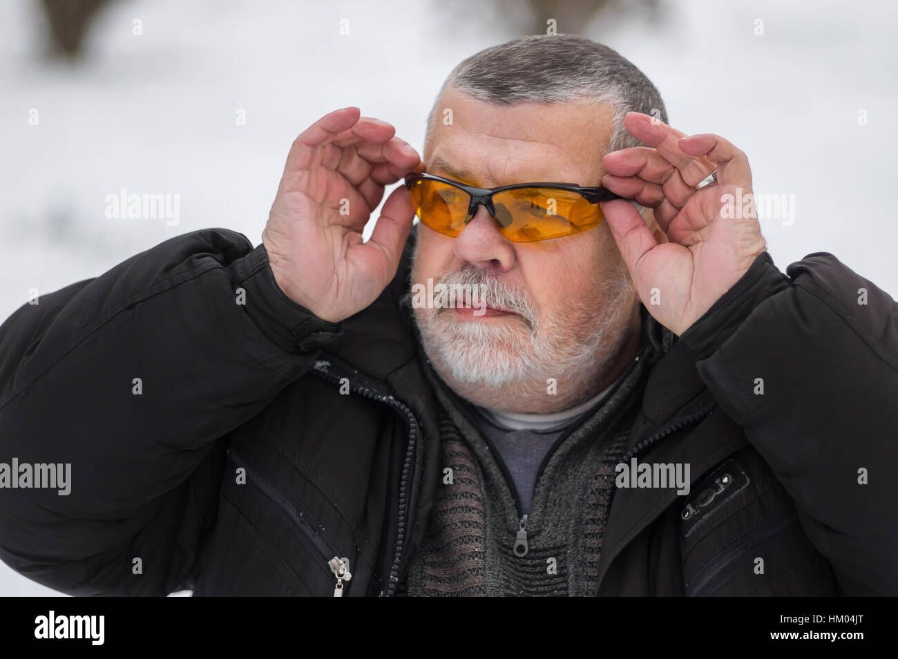 Outdoor ritratto del barbuto caucasica uomo senior regolando gli occhiali da sole a stagione invernale Foto Stock
