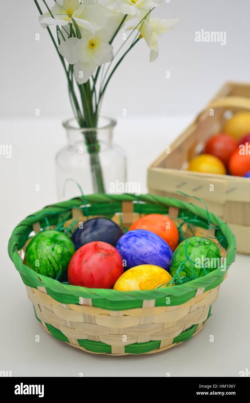 Colorate le uova di Pasqua in un cestino con fiori bianchi su sfondo bianco, close up, verticale Foto Stock