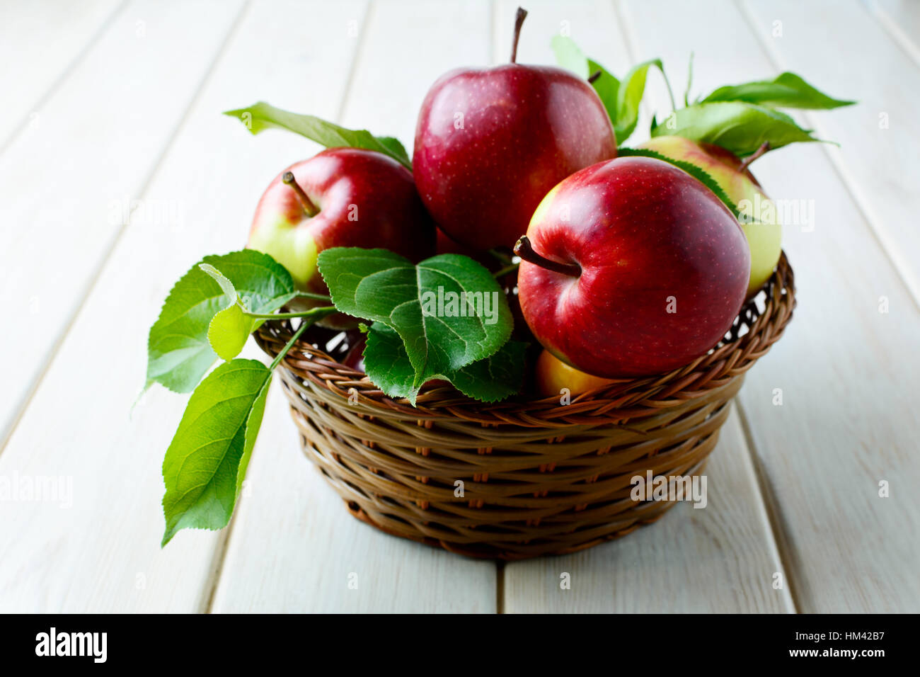 Mele mature con foglie nel cesto su un tavolo di legno. Frutta fresca come mangiare sano concetto. Foto Stock