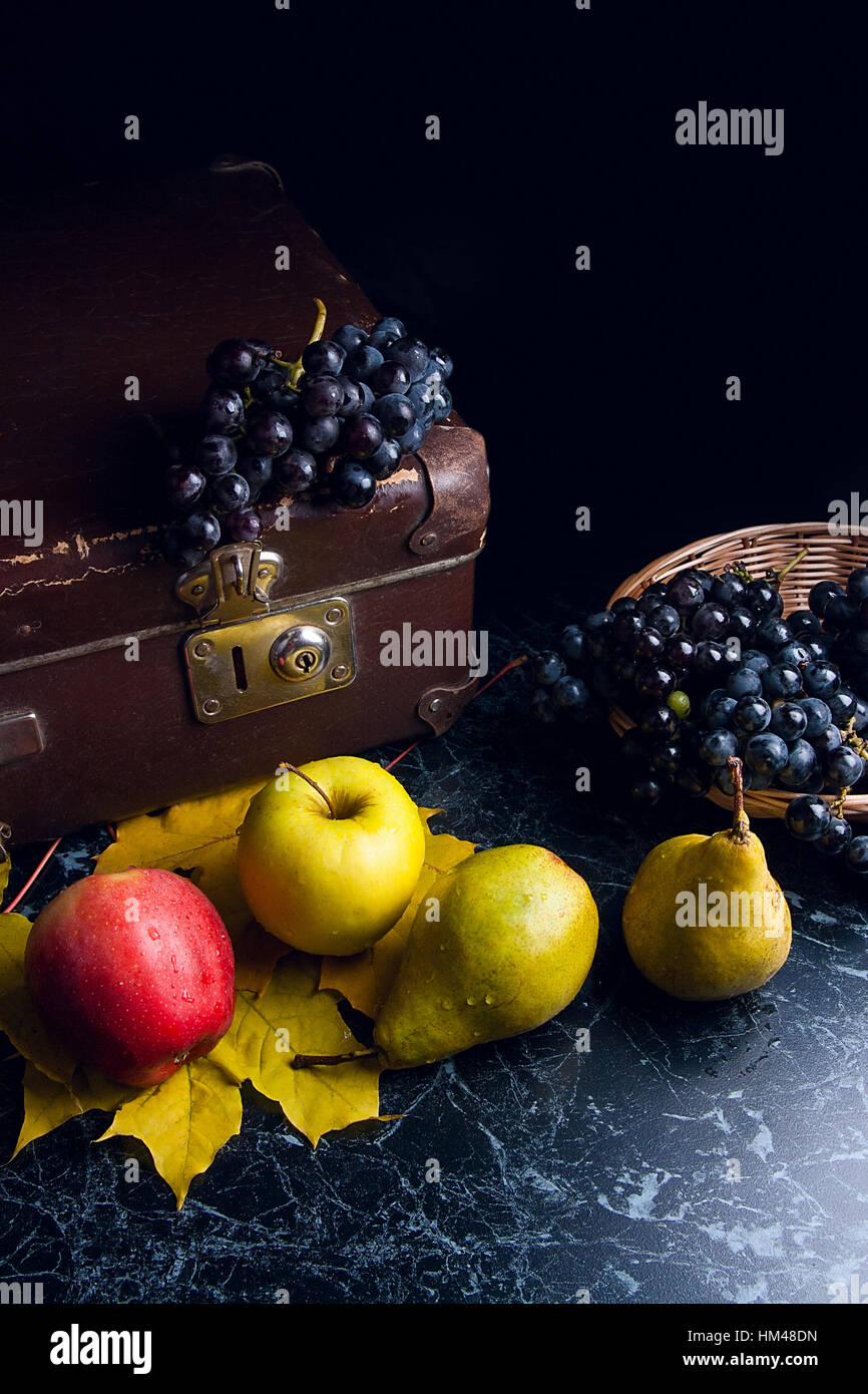 Frutte mature mele, pere e diversi giallo Foglie di autunno sul marmo scuro dello sfondo. L'uva matura nel cestello giallo e il vecchio caso sul retro dello sfondo. Foto Stock