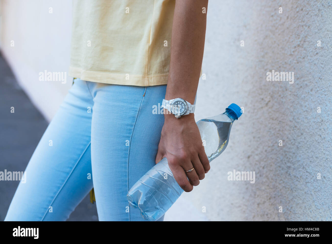 Una bottiglia di acqua potabile in una femmina lato closeup. Una donna in giallo T-shirt e jeans blu tenendo una bottiglia trasparente con acqua. Foto Stock