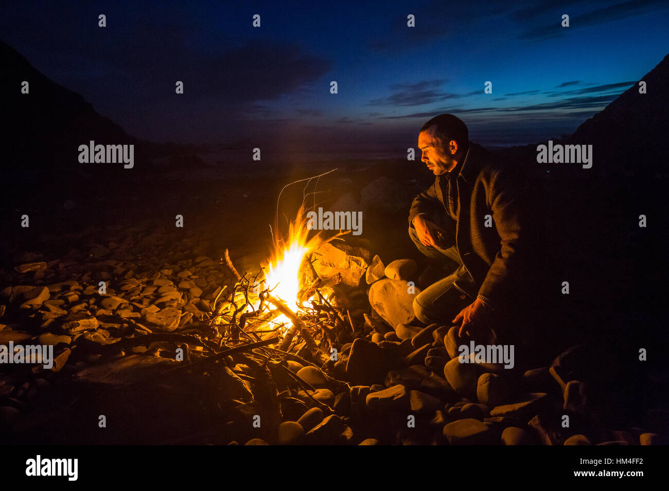 Un uomo solitario stits dal fuoco su una spiaggia deserta in inverno Foto Stock