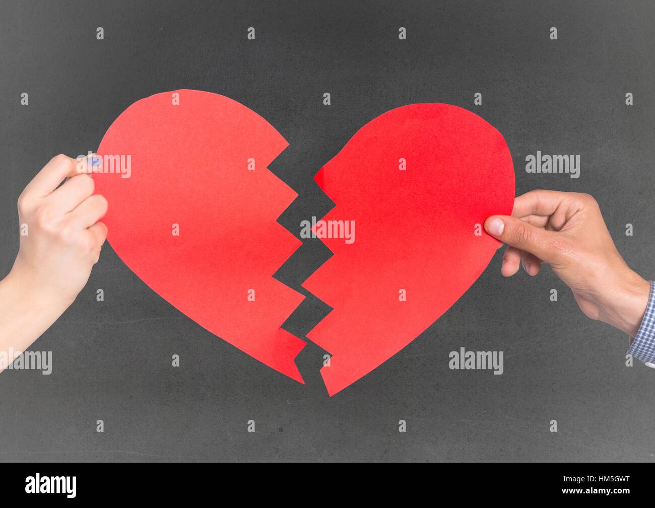 Le mani del giovane azienda cuore spezzato contro uno sfondo grigio Foto Stock
