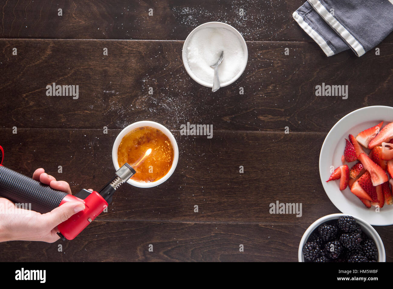 Immagine ritagliata della mano utilizzando la torcia di butano mentre rendendo creme brulee a tavola Foto Stock