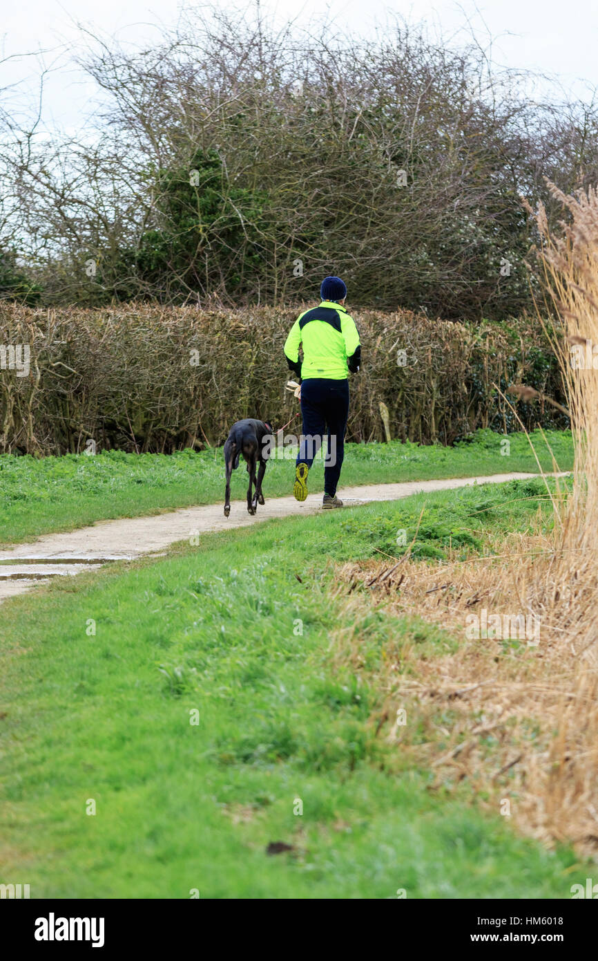 L'uomo jogging con un cane lungo il lato del canale Foto Stock