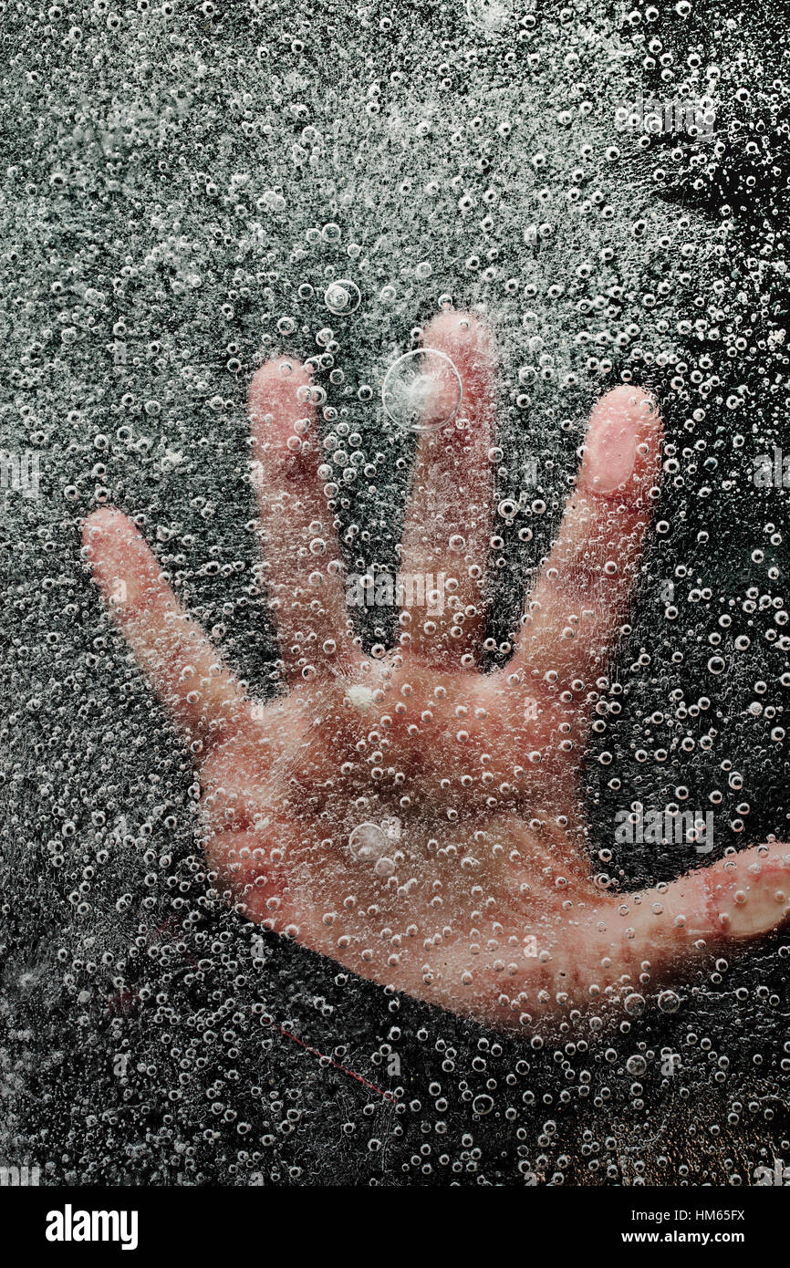 La mano sotto il lago ghiacciato di spingere verso l'alto da sotto il ghiaccio come l uomo è l'annegamento. Lo sfondo scuro e bolle nel ghiaccio. Foto Stock