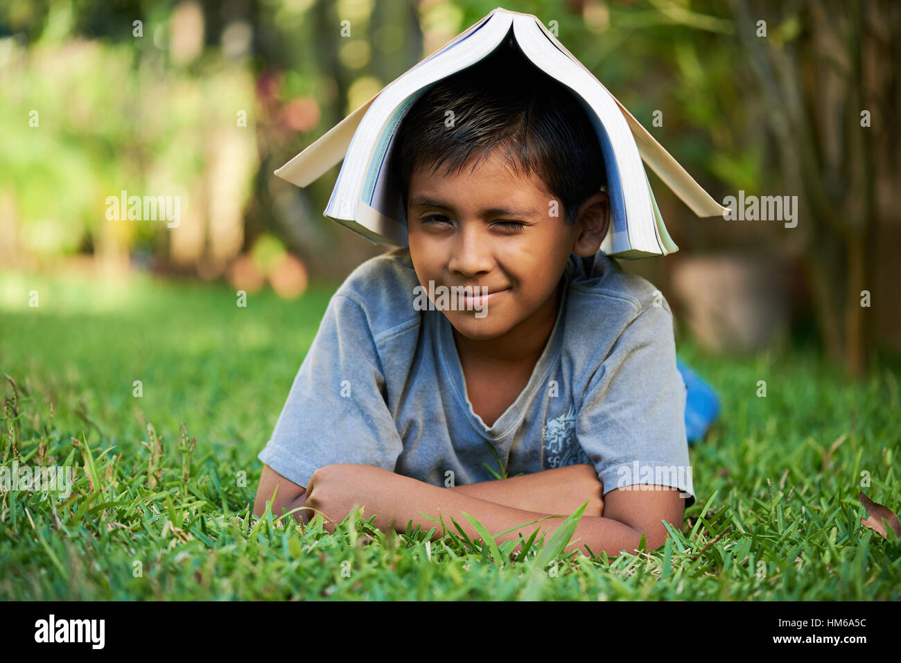 Piccolo sorridente Ragazzo con libro sulla testa i laici sull'erba Foto Stock
