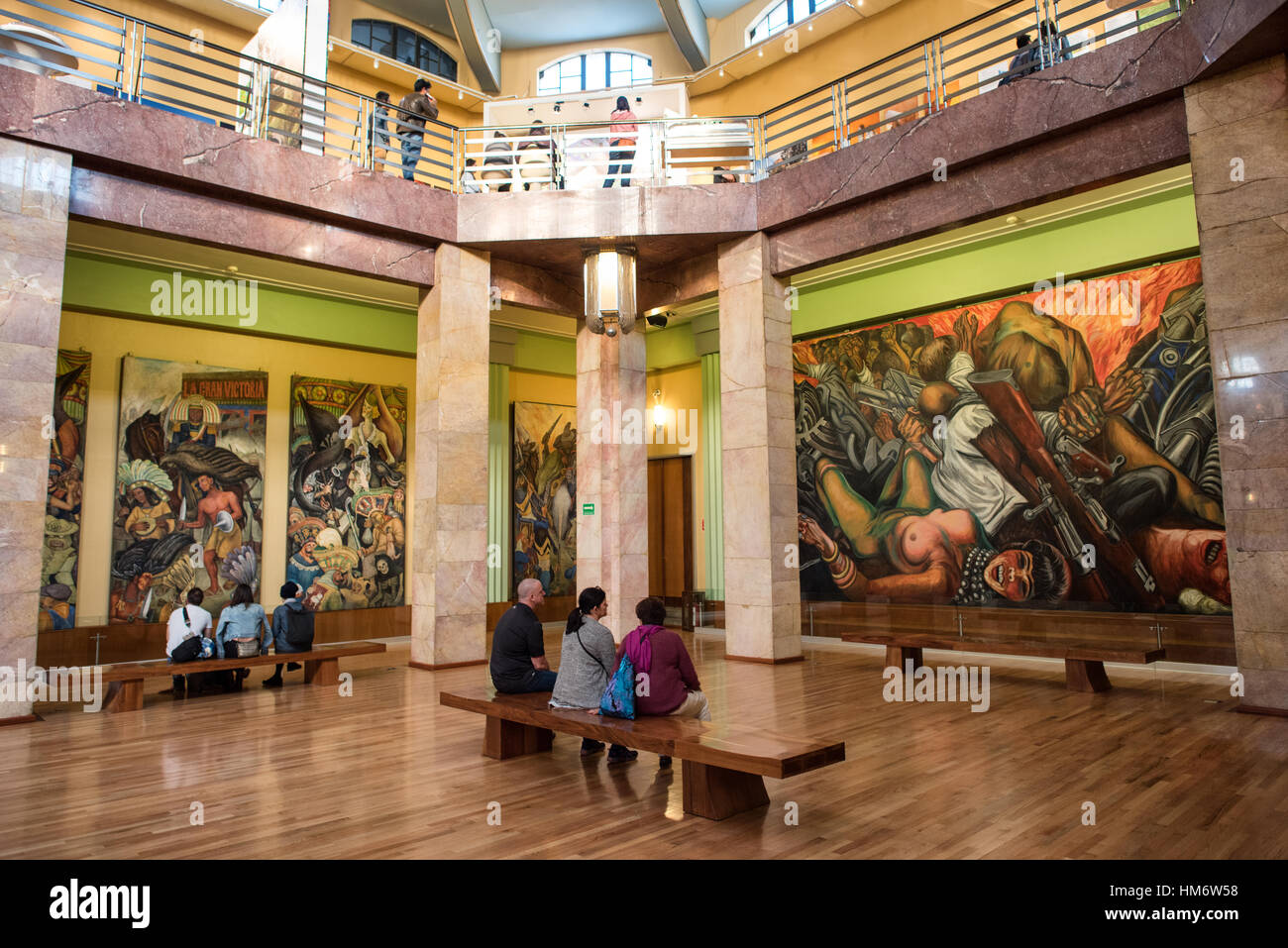 Palacio De Bellas Artes Murals città del Messico // CITTÀ DEL MESSICO, Messico - i visitatori si siedono per vedere i murales del Palacio de Bellas Artes, che ospita la più importante collezione di murales messicani dei più grandi artisti messicani del XX secolo. Queste opere monumentali includono capolavori di Diego Rivera, David Alfaro Siqueiros, José Clemente Orozco e Rufino Tamayo. I murales, creati tra il 1920 e il 1950, raffigurano temi fondamentali del nazionalismo messicano, della giustizia sociale e dell'identità culturale. Il Palacio de Bellas Artes, completato nel 1934, è il principale luogo culturale del Messico e l'opera hous Foto Stock
