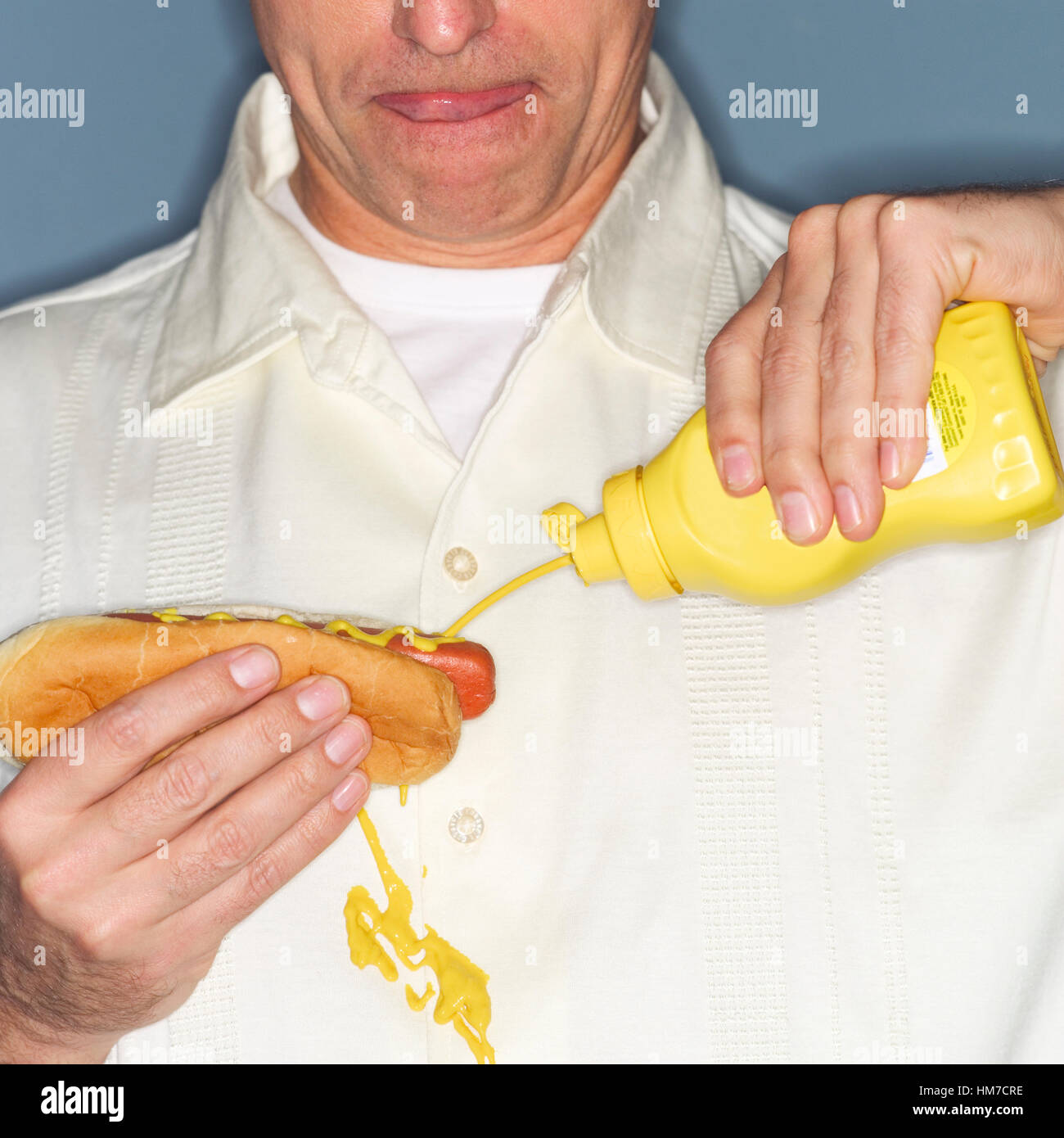 Uomo maturo holding hotdog e fuoriuscita accidentalmente la senape sulla camicia Foto Stock