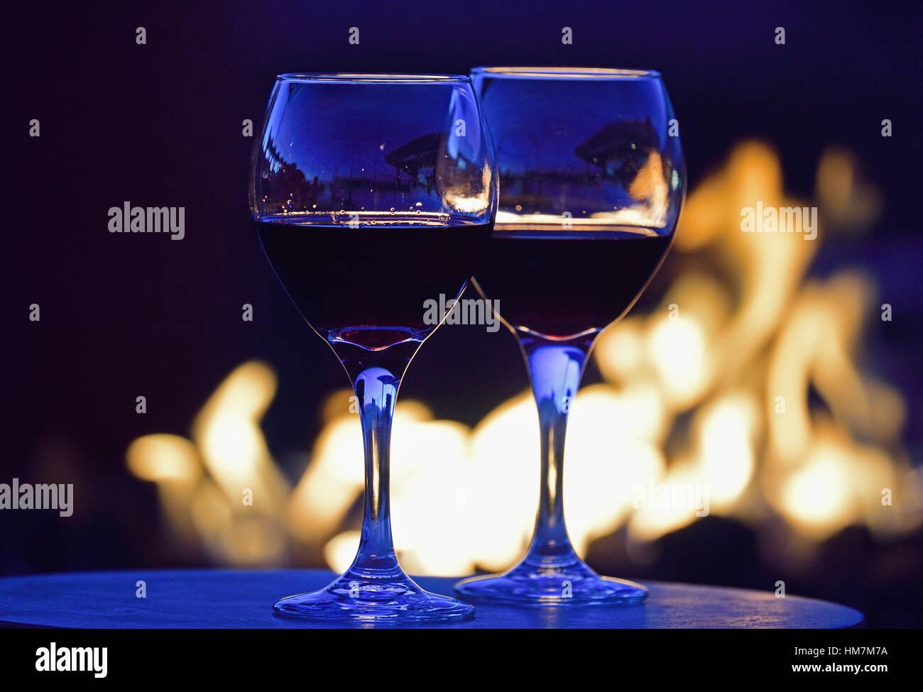 Bicchieri di vino rosso contro una buca per il fuoco di notte Foto Stock