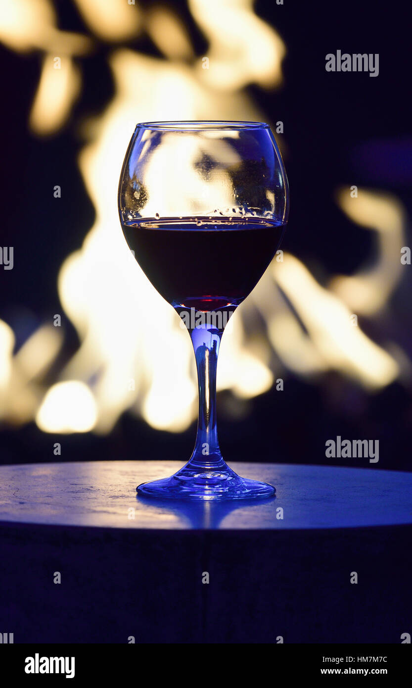 Bicchiere di vino rosso contro una buca per il fuoco di notte Foto Stock