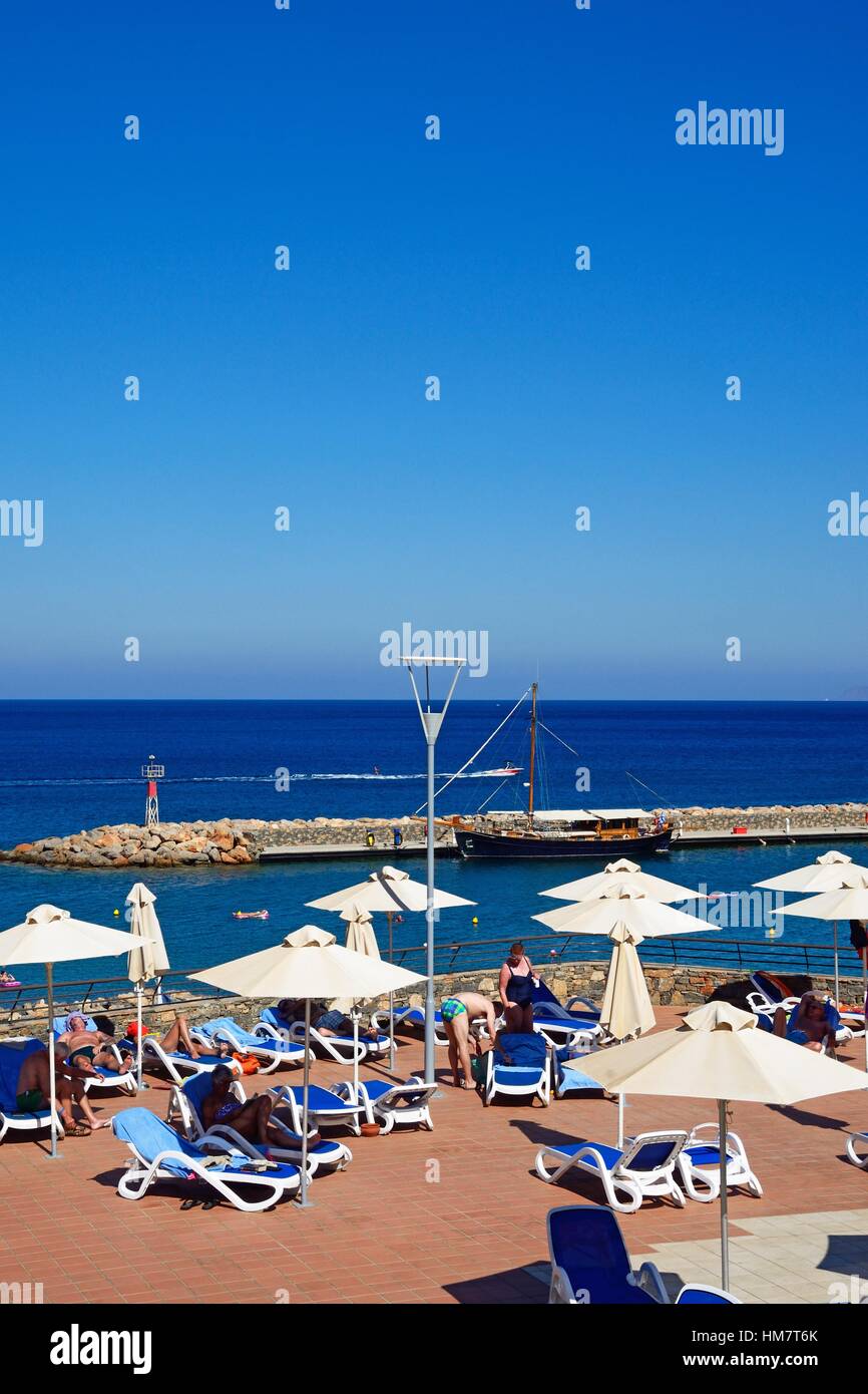 I turisti la rilassante Hotel Mirabello terrazza per prendere il sole con il porto verso la parte posteriore, Agios Nikolaos, Creta, Grecia, l'Europa. Foto Stock