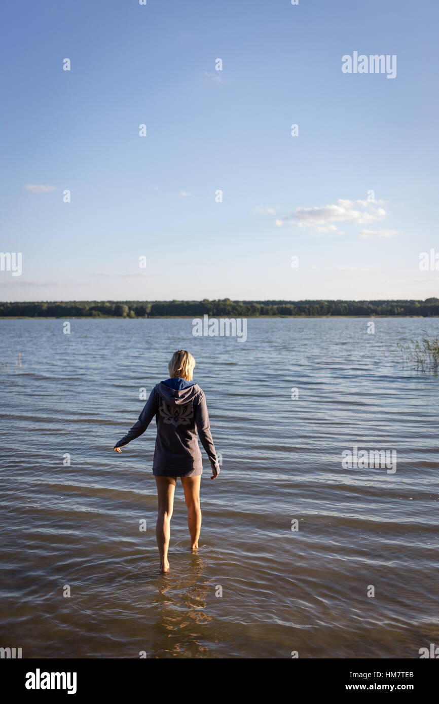 Una donna con capelli biondi wading o sguazzare attraverso acqua, lago Foto Stock