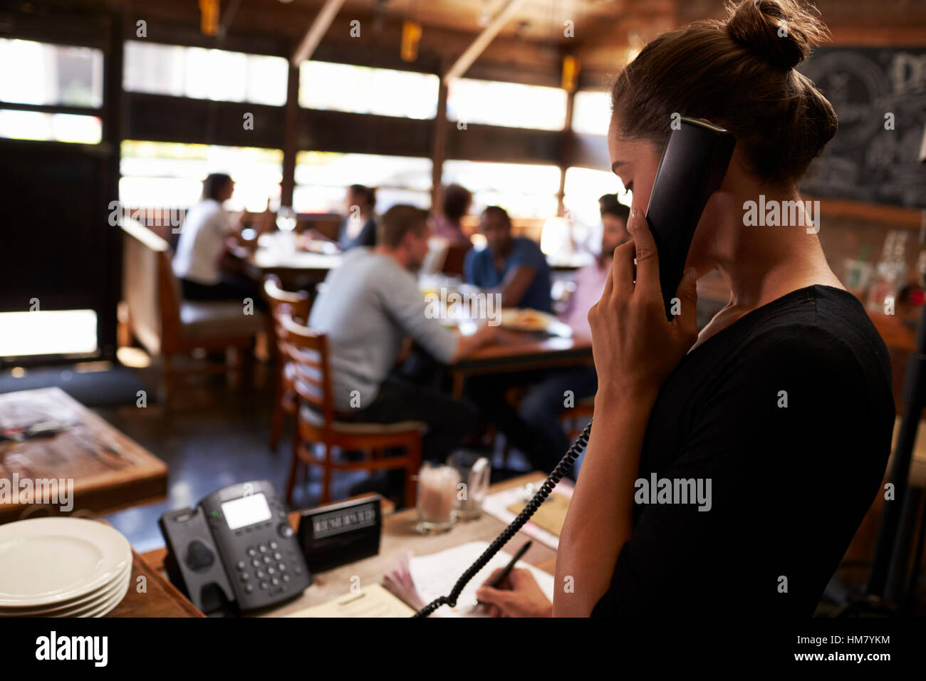Giovane donna prendendo una prenotazione per telefono presso un ristorante Foto Stock