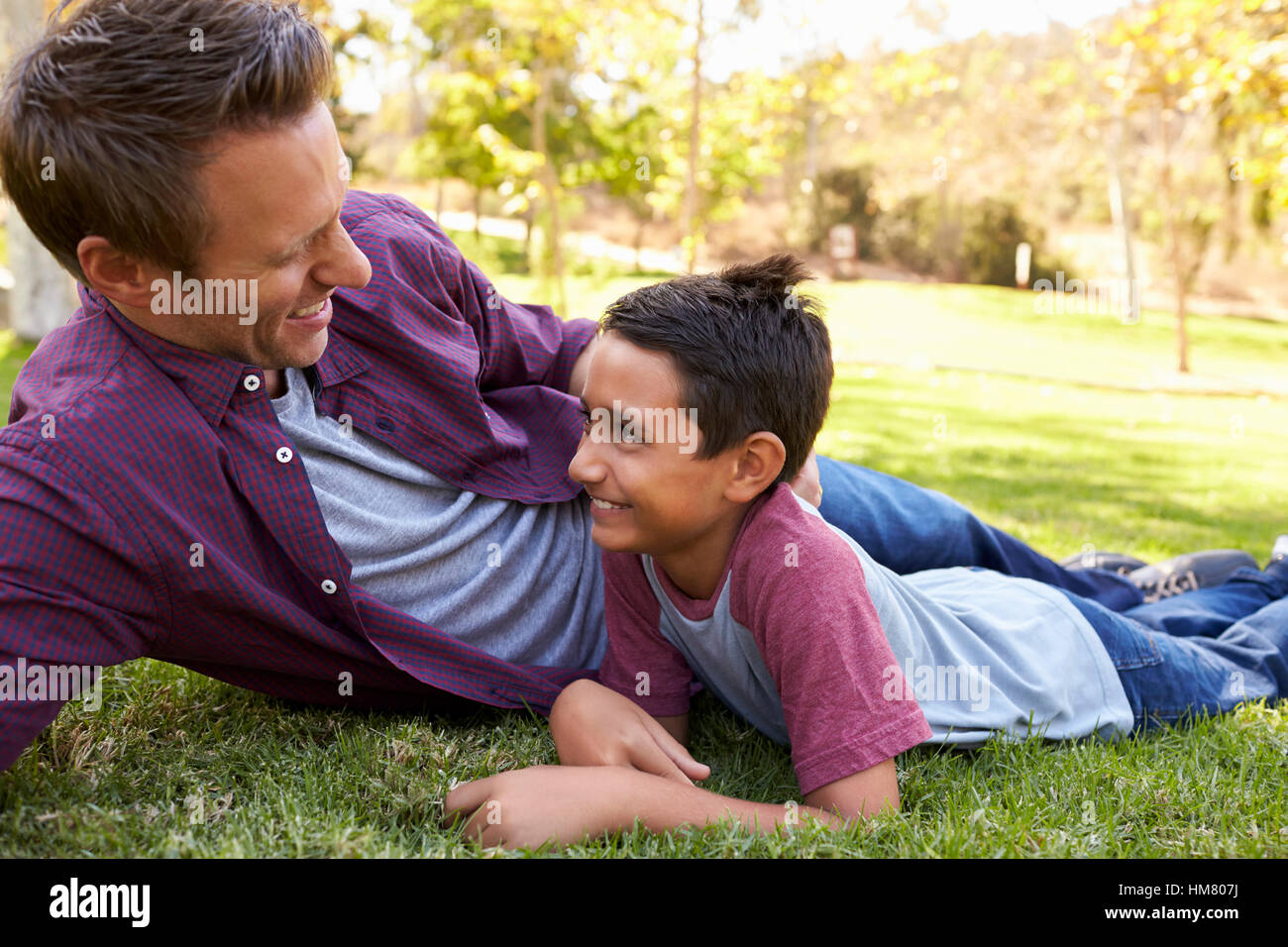 Gara di misto ragazzo asiatico giacente in un parco con il suo padre bianco Foto Stock