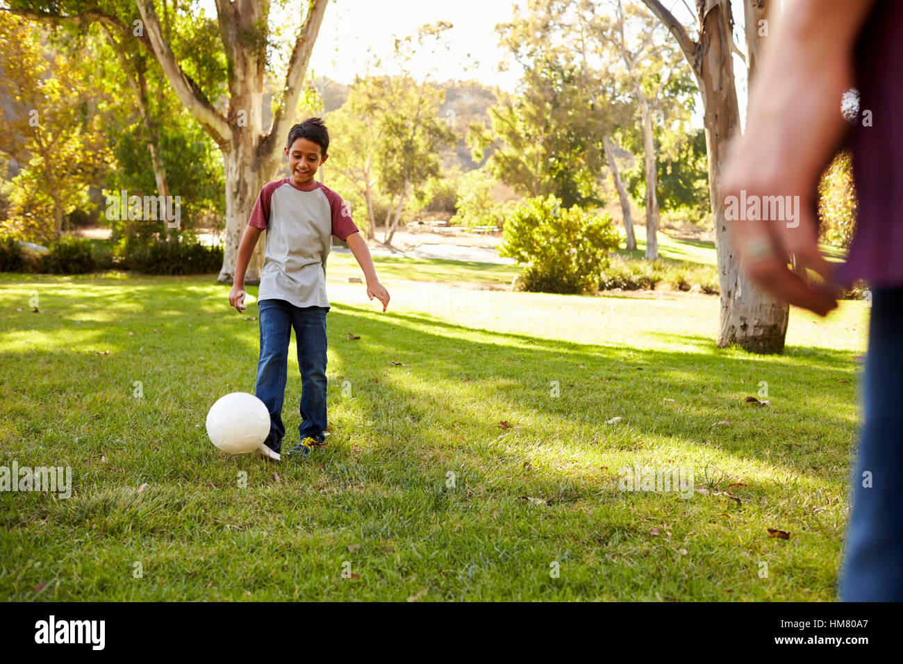 Sette anni di vecchio ragazzo giocando a calcio in un parco con papà Foto Stock
