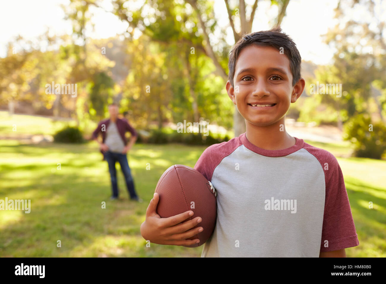 Ritratto di ragazzo tenendo il calcio nel parco, papà in background Foto Stock