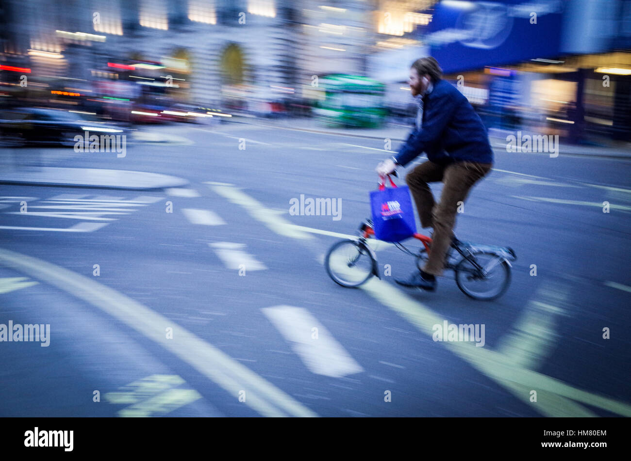 Un ciclista su una Brompton bicicletta pieghevole attraversa Piccadilly Circus a Londra centrale - sfocatura del movimento Foto Stock