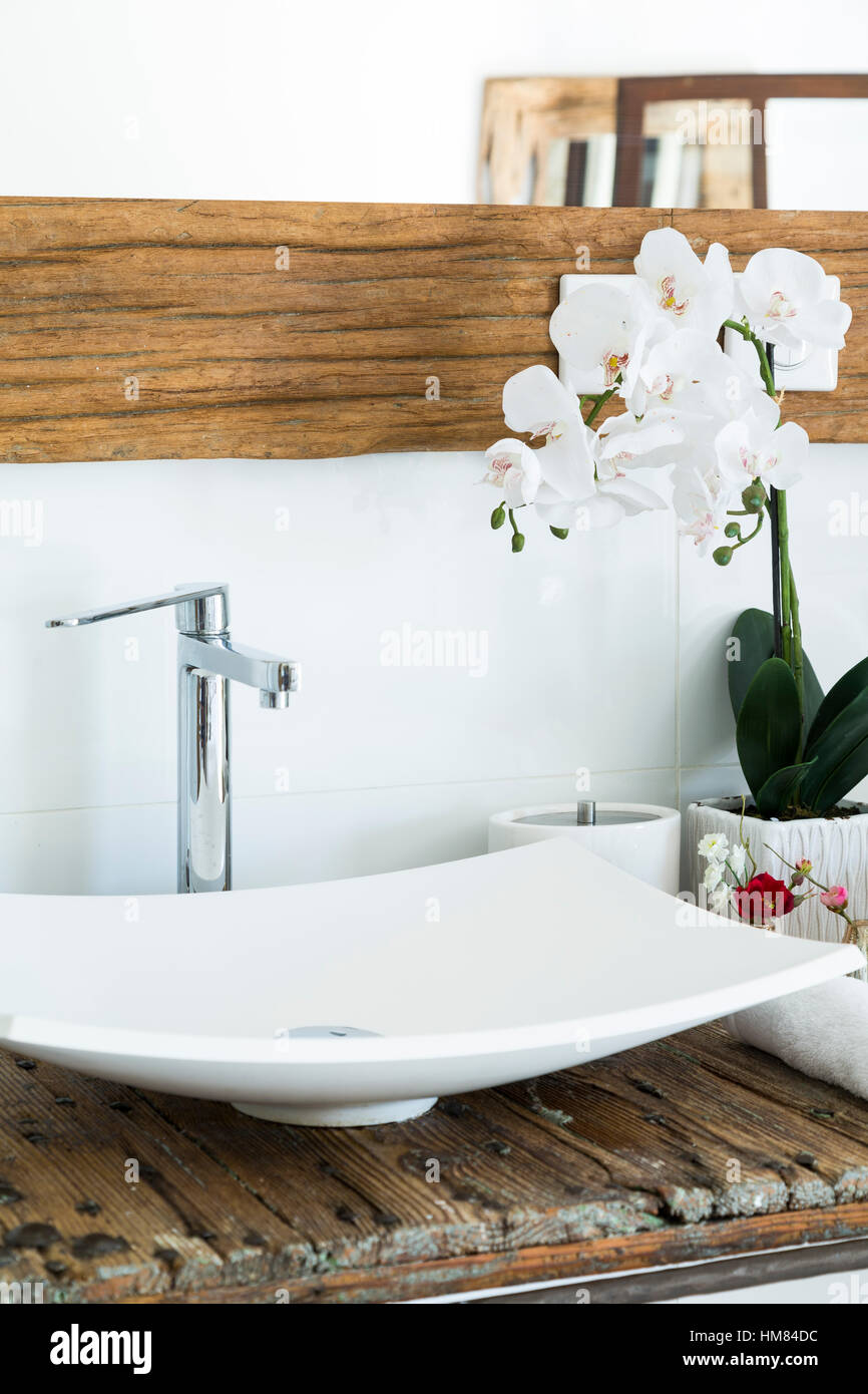 Moderno bagno lavandino con rubinetto cromato specchio in legno bianco e la tignola fiori di orchidea Foto Stock