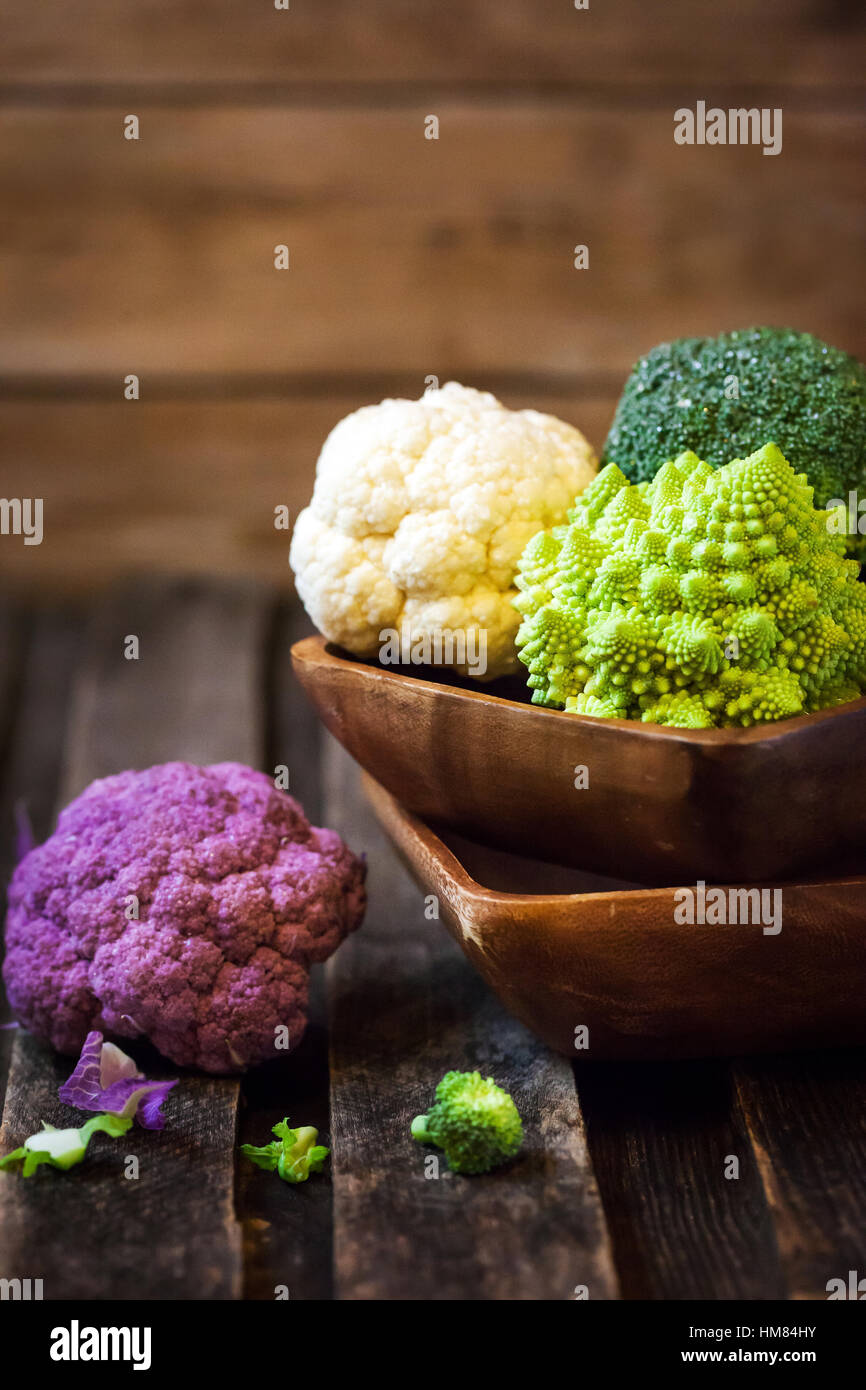 Organico fresco bianco e viola cavolfiori, broccoli, romanesco nella ciotola di legno Foto Stock