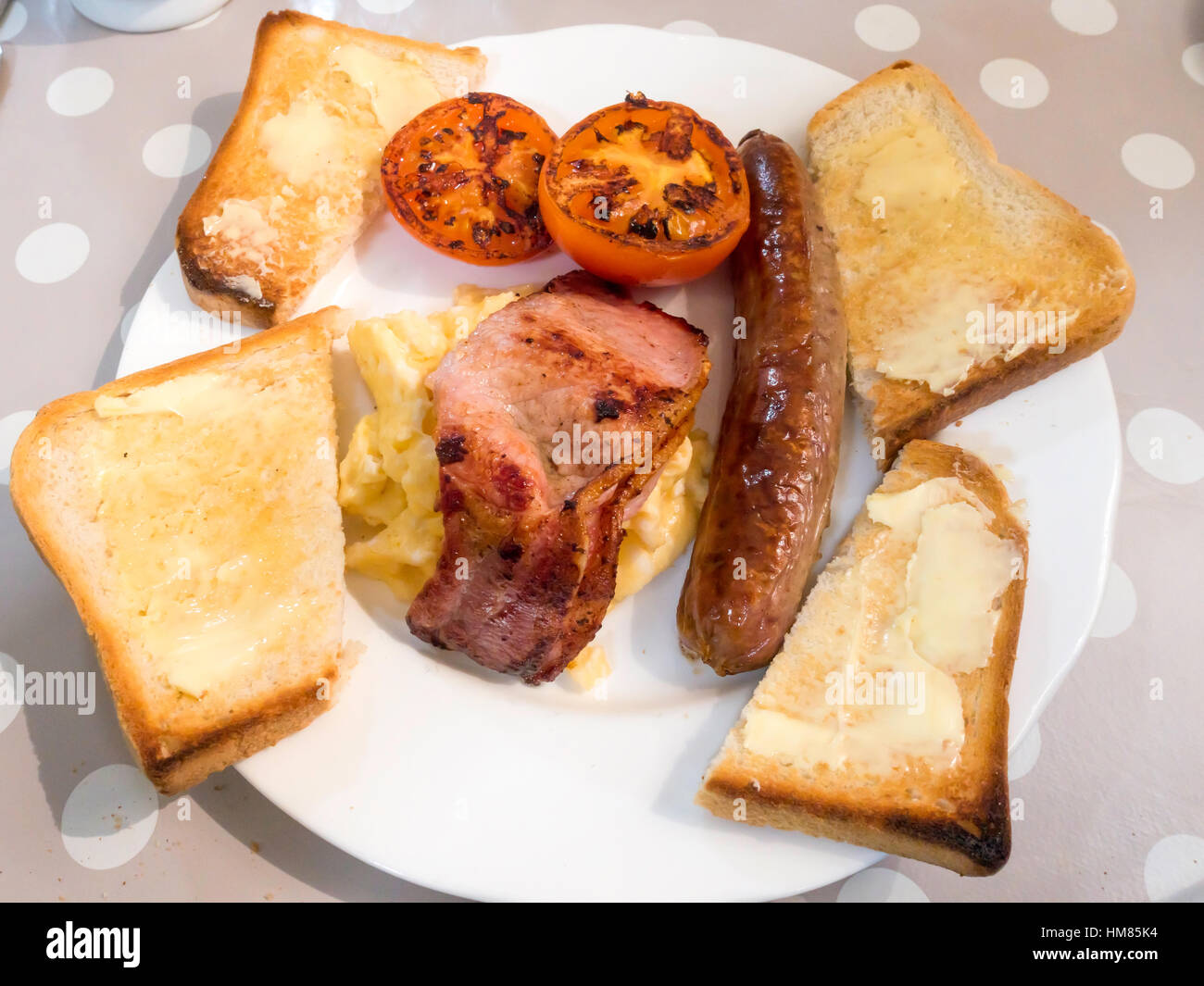 Café pasto una piccola prima colazione inglese con bacon uova strapazzate, salsiccia e pomodoro fritto servito con toast bianchi Foto Stock