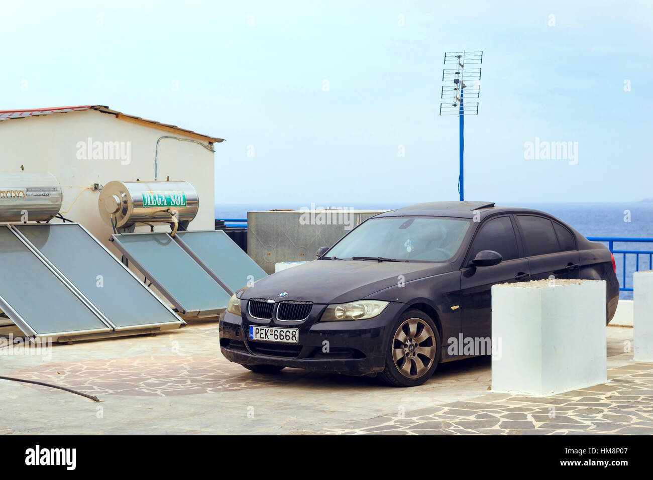 Bali, Grecia - 30 Aprile 2016: Contemporanea sportivo nero BMW auto parcheggiate sul terrapieno accanto a pannelli solari con acqua caldaie di riscaldamento. Villaggio turistico Foto Stock