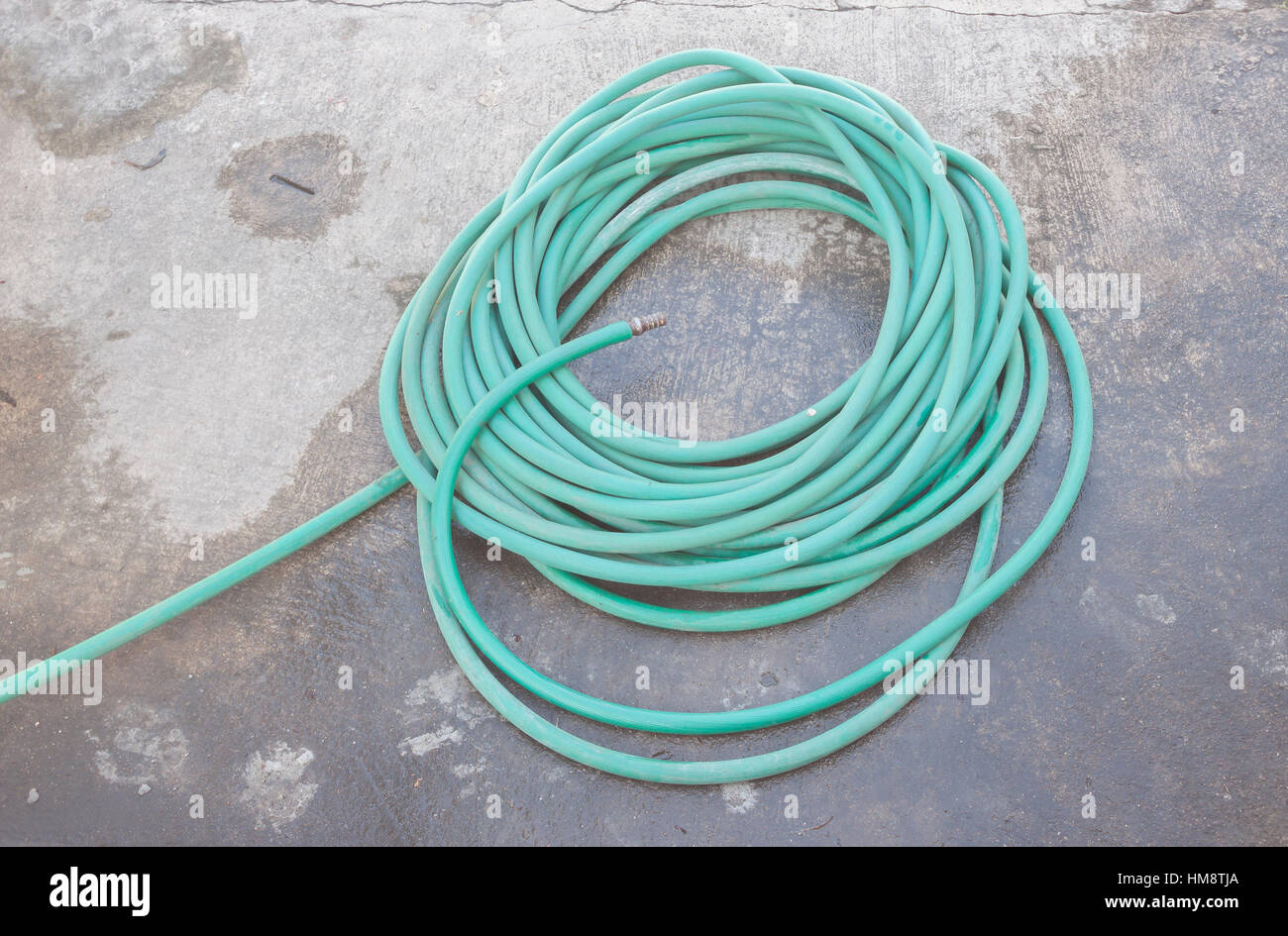 Tubo di gomma per innaffiare le piante su pavimento bagnato Foto Stock