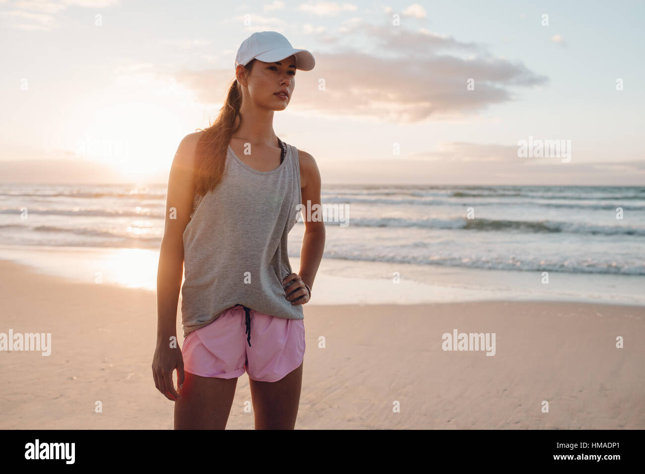 Colpo di modello di fitness in sportswear permanente sulla spiaggia con la sua mano sull'anca. Sano giovane donna sulla riva del mare nella mattina. Foto Stock