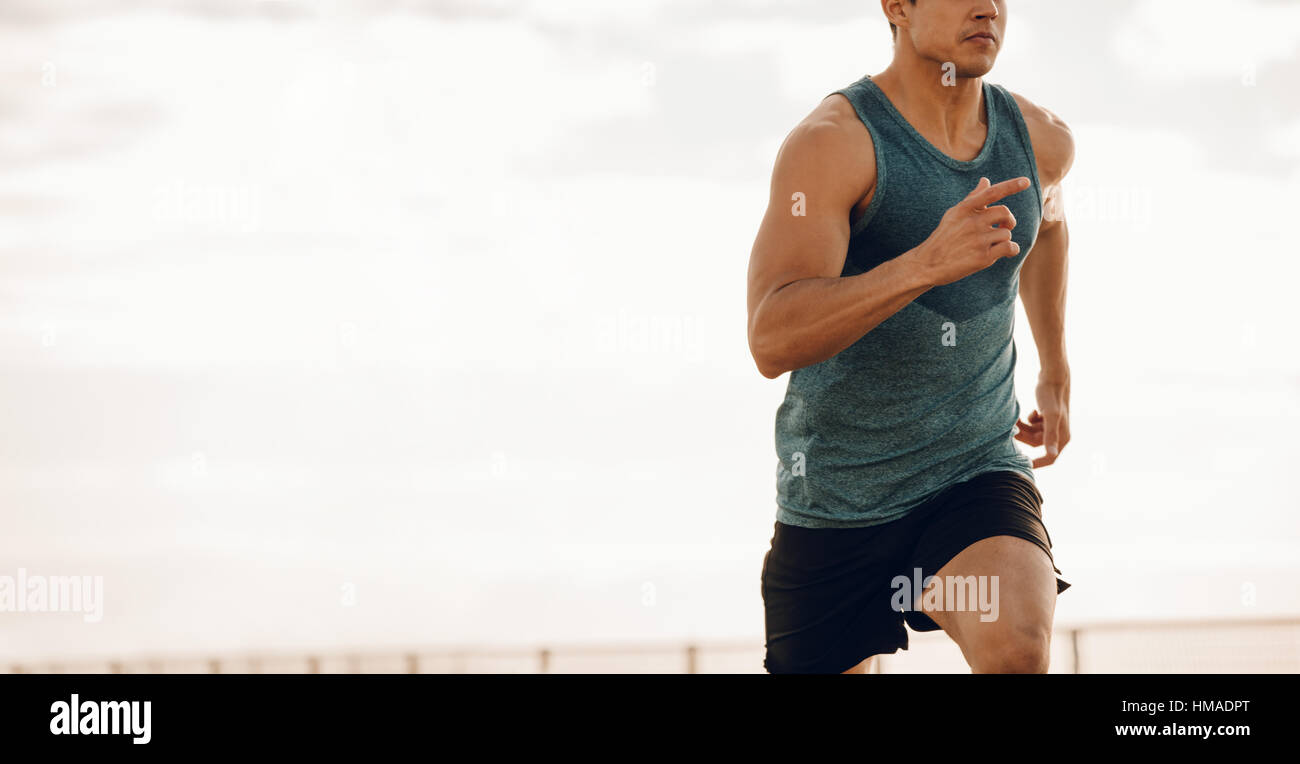 Ritagliato shot del giovane uomo che corre lungo una passeggiata sul lungomare. Sani e giovani runner maschio lavoro su una strada sul mare. Foto Stock