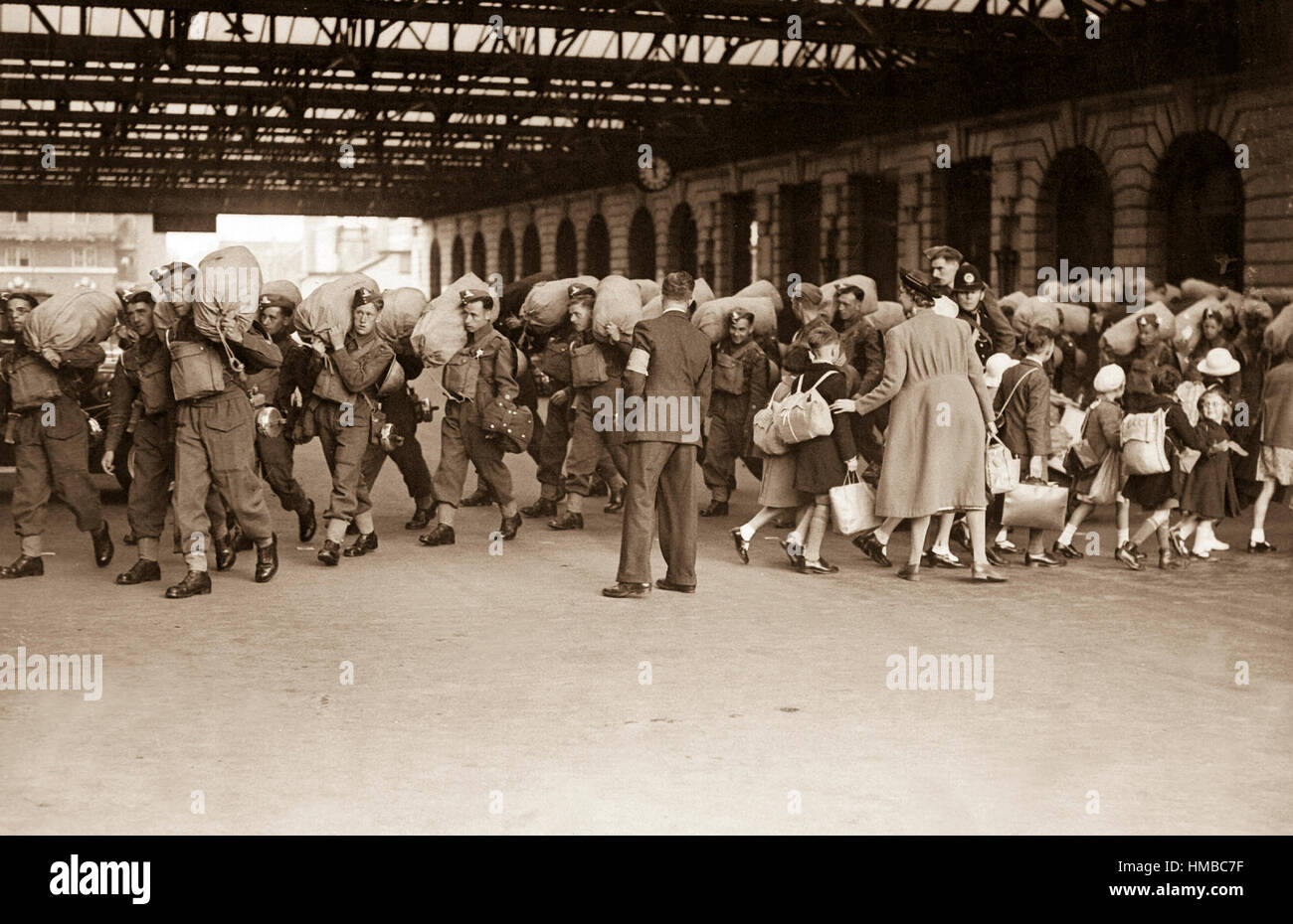 Una scena a un alla stazione ferroviaria di Londra che mostra le truppe in arrivo mentre i bambini che sono stati evacuati da Londra per lasciare la zona della reception. Ca. 1940. Foto Stock