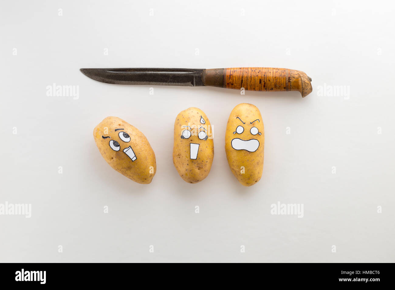 Patate fresche con stile cartoon facce posa sulla superficie bianca sono spaventati da un coltello Foto Stock