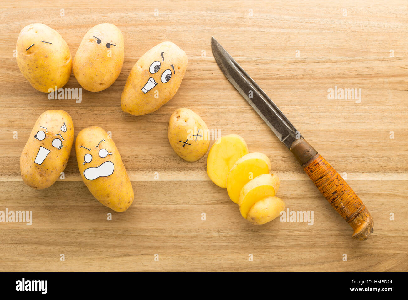 Patate fresche con stile cartoon facce posa su un marrone tagliere e spaventato a morte da un coltello Foto Stock