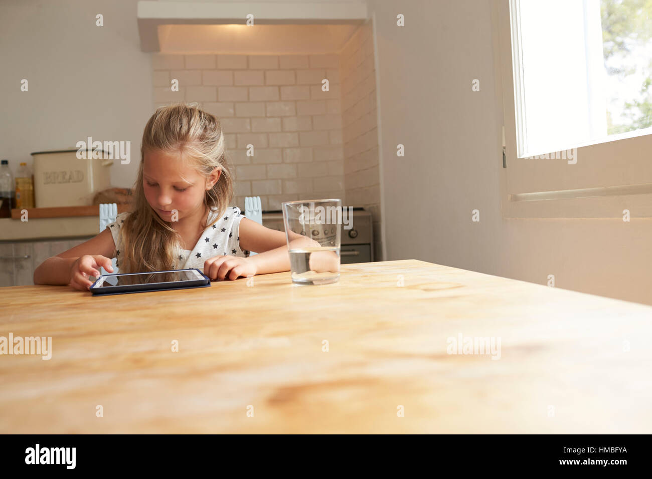 Giovane ragazza a casa utilizzando la tavoletta digitale sul tavolo da cucina Foto Stock