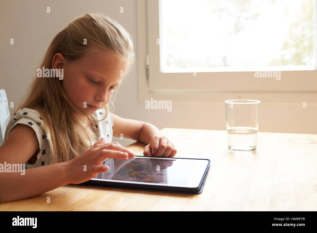 Giovane ragazza a casa utilizzando la tavoletta digitale sul tavolo da cucina Foto Stock