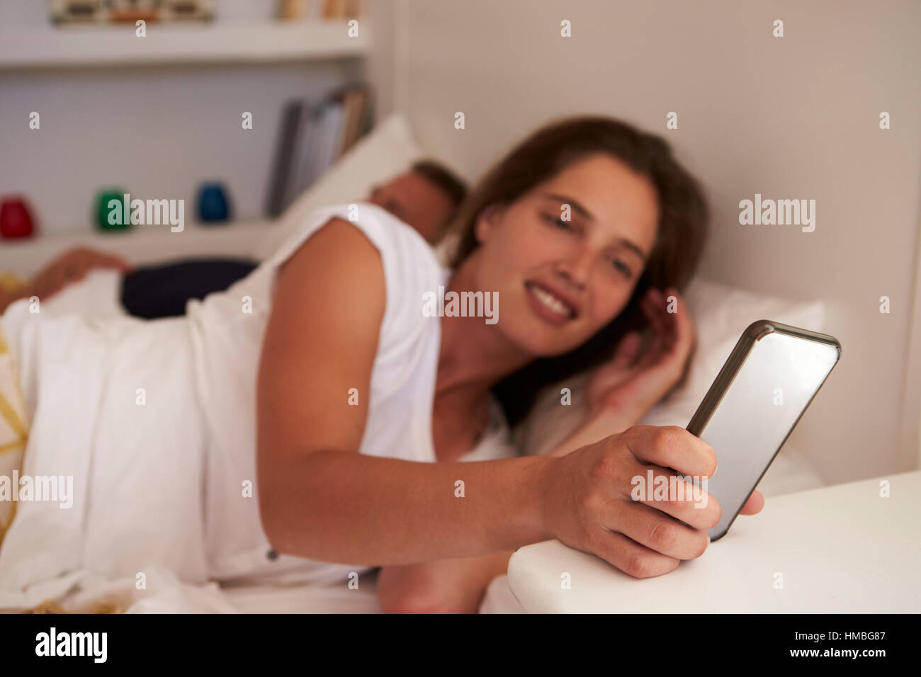 La donna nel letto dello smartphone utilizza, partner dorme, concentrarsi sul telefono Foto Stock