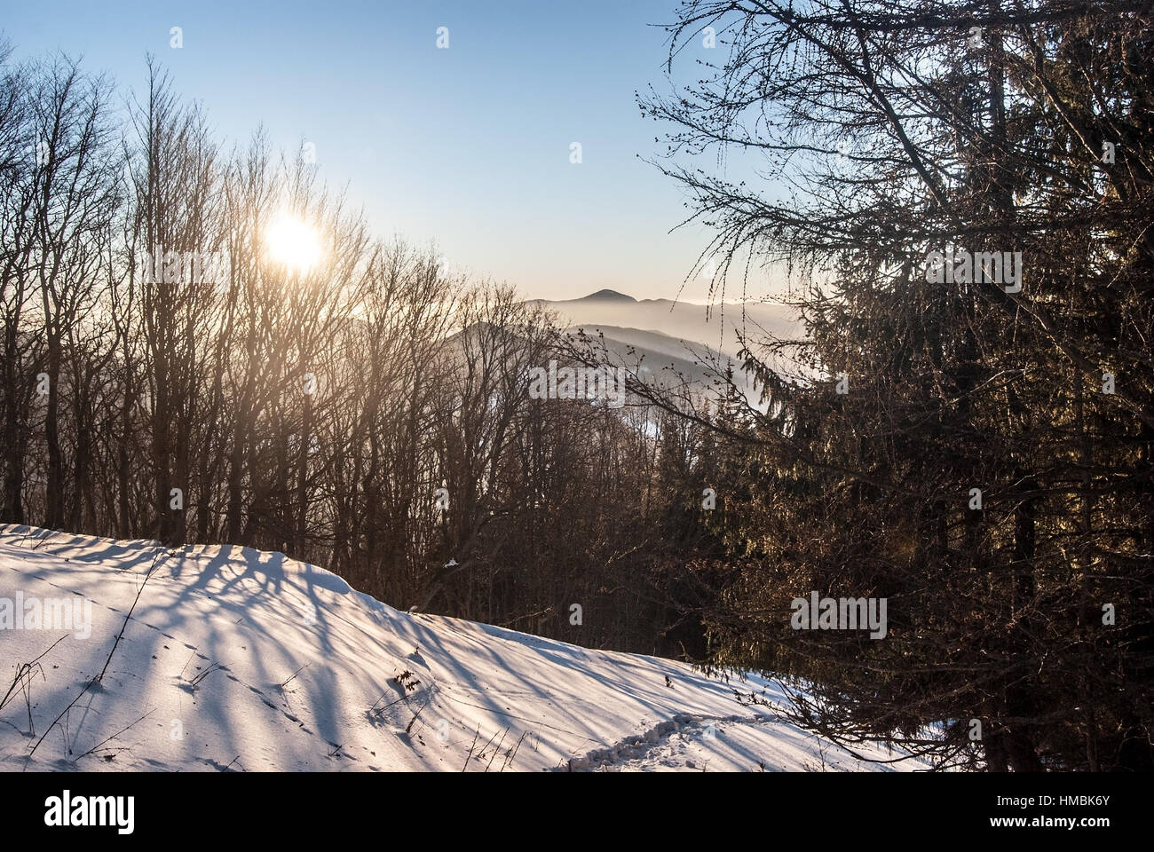 Tramonto in inverno in mala fatra mountaine bellow maly klak collina con neve, alberi, sun, colline con nebbia sullo sfondo e il cielo chiaro Foto Stock