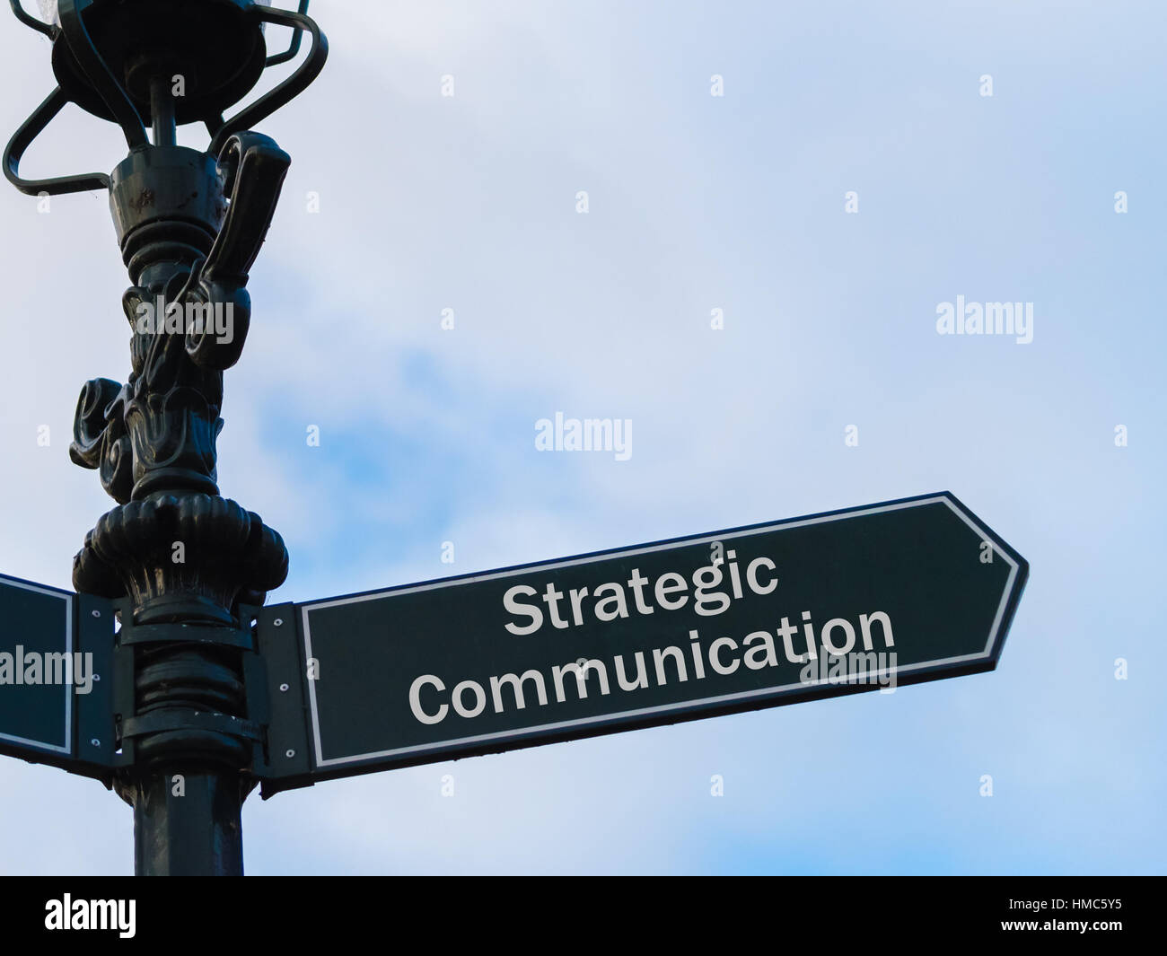 Illuminazione stradale pole con messaggio concettuale comunicazione strategica sulla freccia direzionale blu su sfondo nuvoloso. Foto Stock