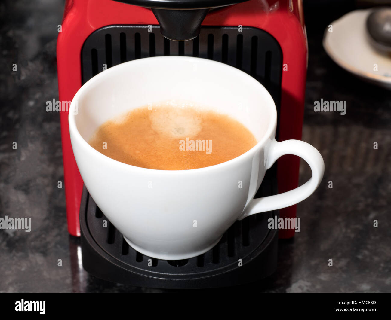 Un bianco tazza di caffè che mostra un espresso crema seduto su un rosso caffè Nespresso capsule macchina Foto Stock