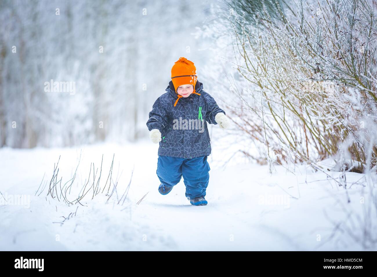 Felice ragazzo giocando all'aperto in inverno. Bambino caucasico in arancione hat e vestiti caldi a giocare all'aperto in inverno. Foto Stock