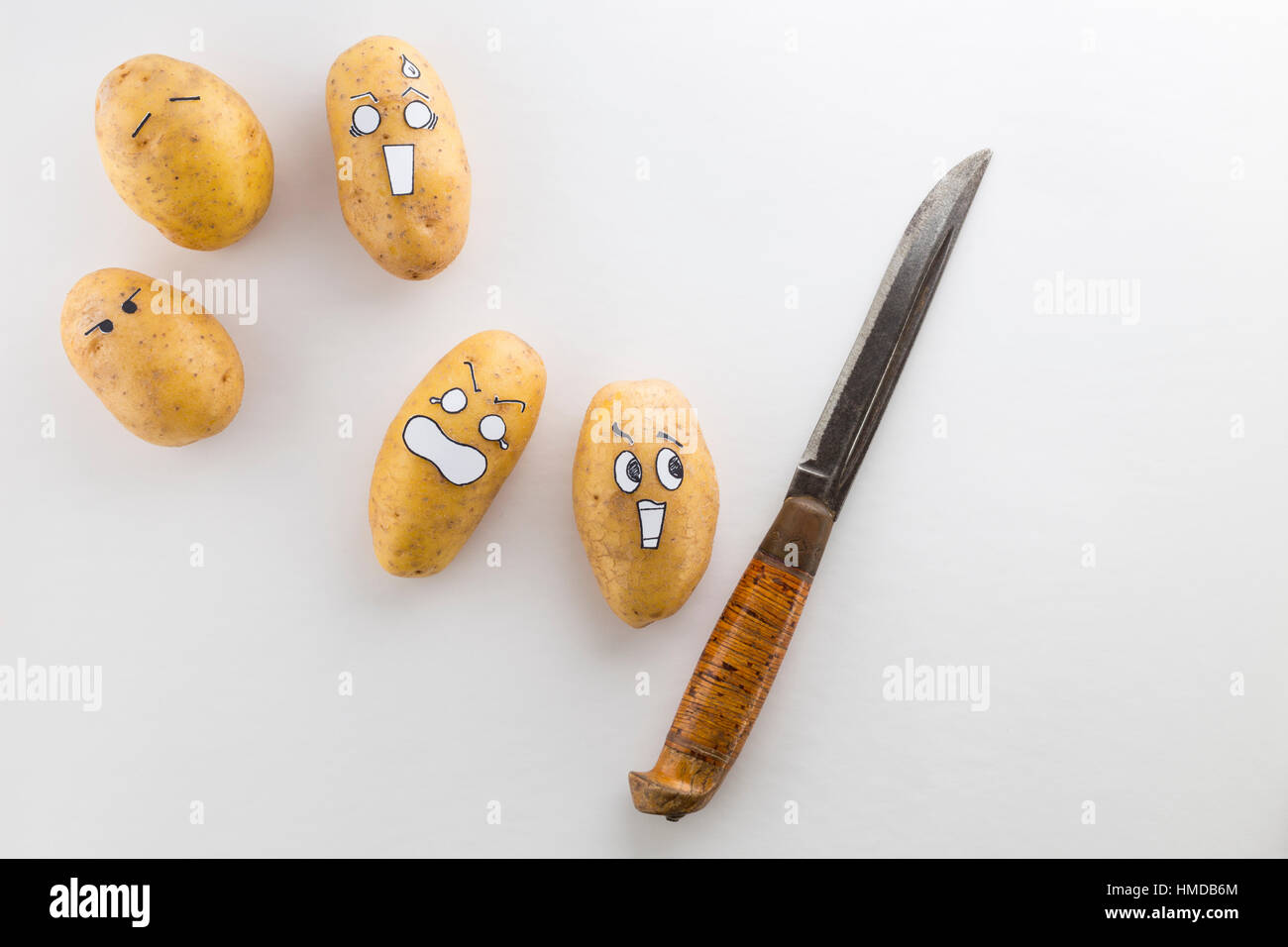 Patate fresche con stile cartoon facce posa sulla superficie bianca sono spaventati da un coltello Foto Stock