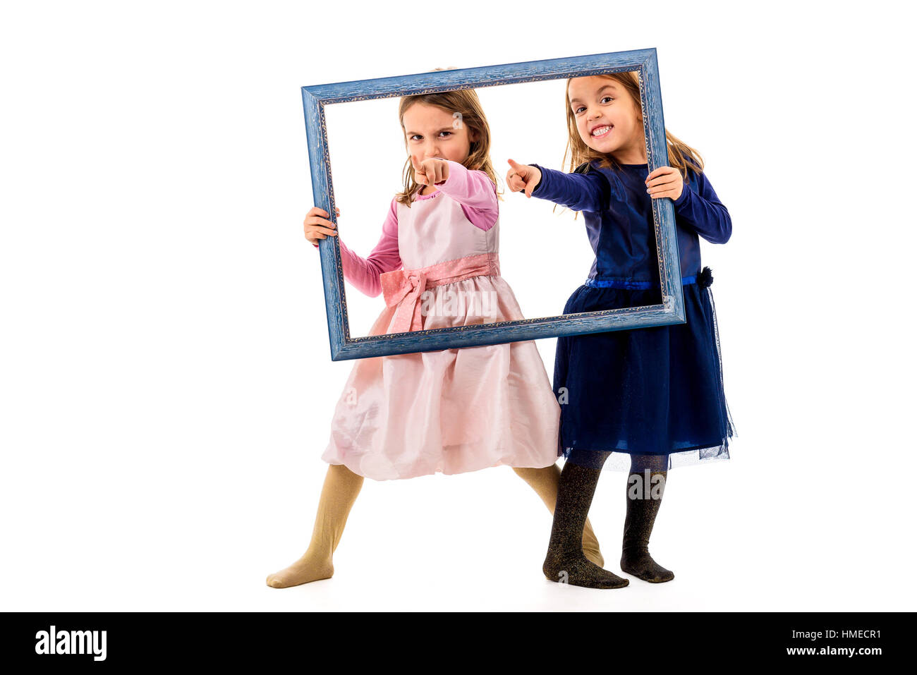 Due gemelle sono rivolti con le dita tenendo cornice immagine. I bambini in posa di studio, ingannare intorno a produrre diverse espressioni del viso e puntamento Foto Stock