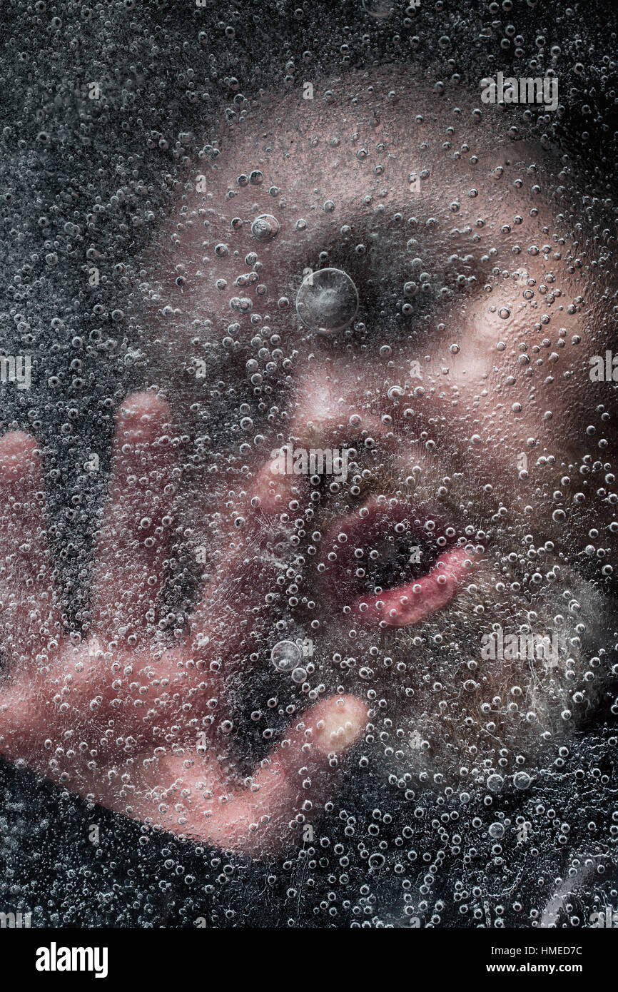 L'uomo faccia chiudere fino annegamento in un lago ghiacciato con uno sfondo scuro. Lo strato di ghiaccio con bolle copre l'acqua contro uno sfondo scuro Foto Stock