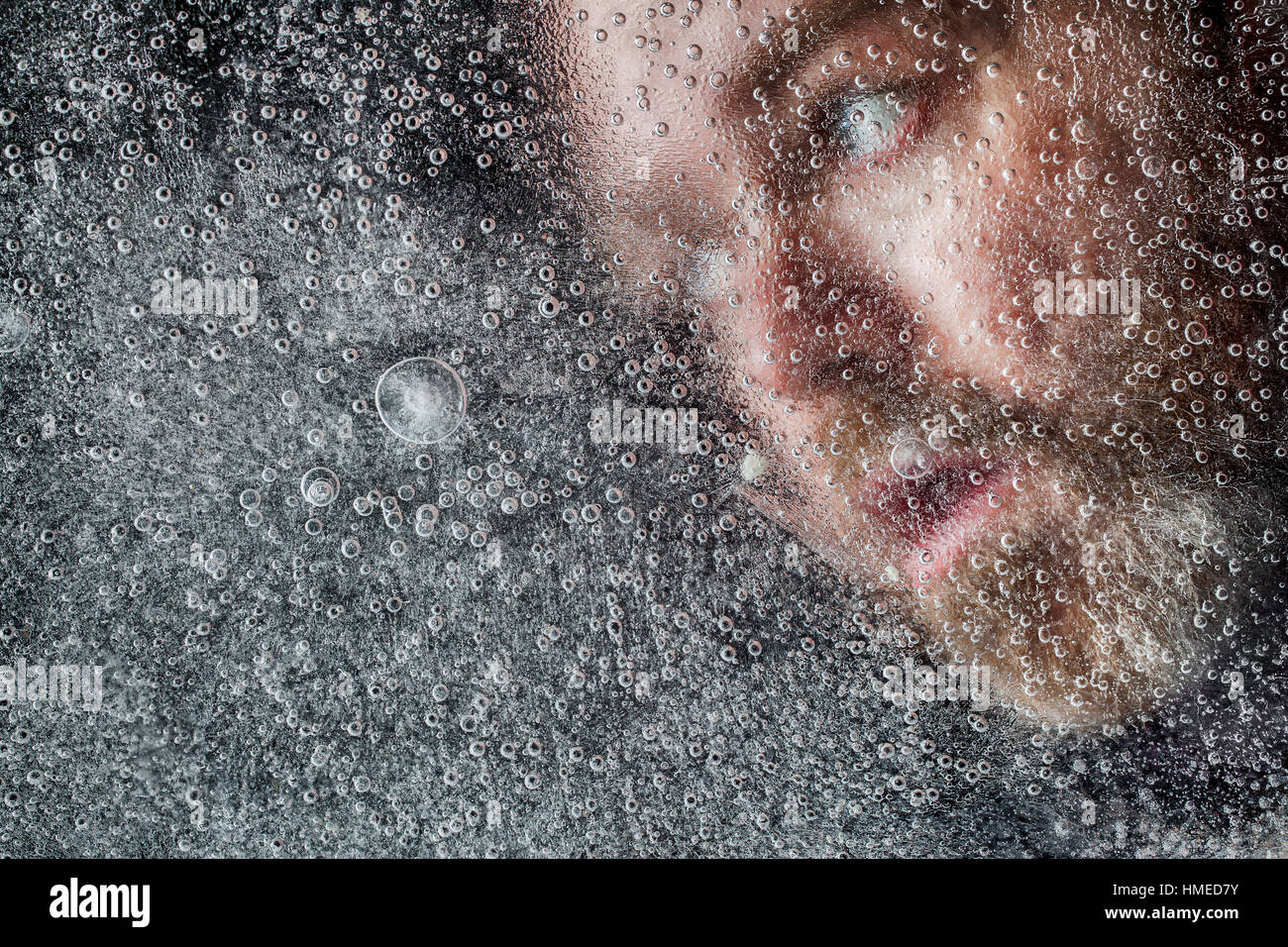 L'uomo annegamento in un lago ghiacciato coperto con uno spesso strato di ghiaccio. Aprire gli occhi e la bocca con la barba contro uno sfondo scuro Foto Stock