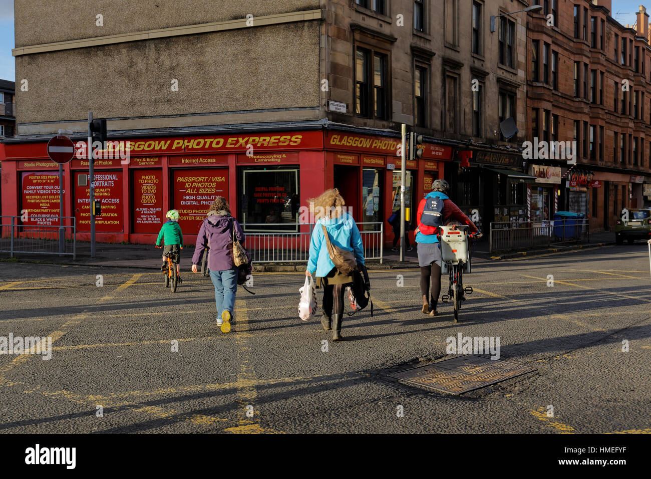 Ciclista middle class bianchi attraversamento strada come una famiglia Govanhill, Glasgow, Scotland, Regno Unito Foto Stock